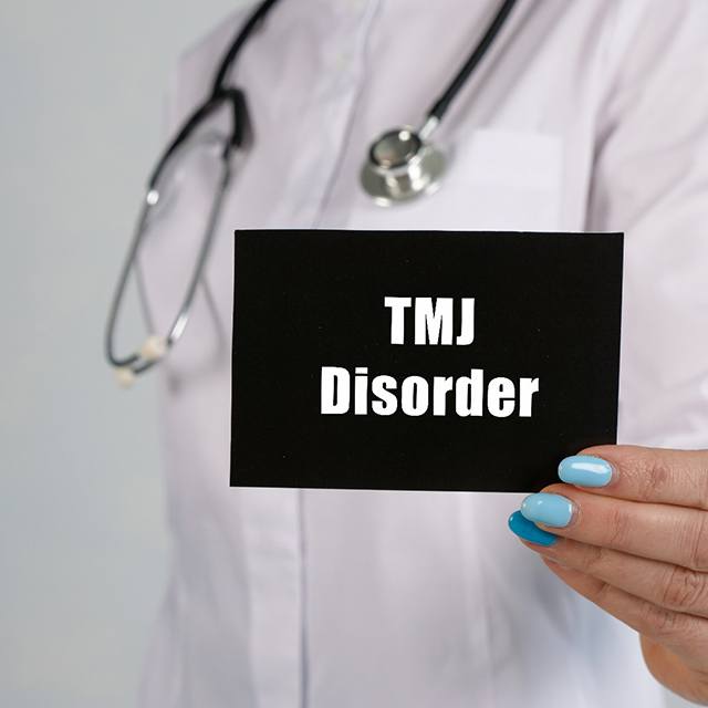 Medical professional holding sign that says, “TMJ Disorder”