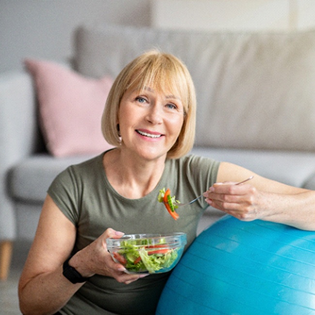 Healthy senior woman eating salad with help of implant dentures