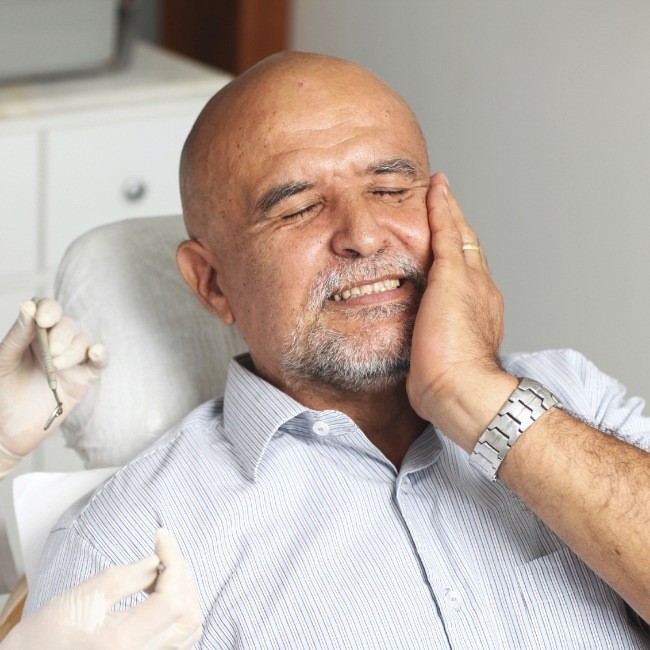 Man in need of dental emergency treatment holding cheek in oral surgery office