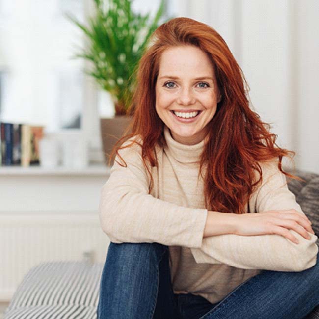 Smiling woman with dental implants sitting on sofa