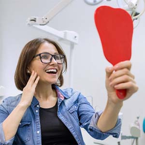 Dental patient using mirror to admire her new implant restorations