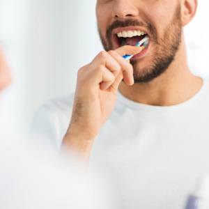 Man brushing teeth in front of mirror, caring for his dental implants