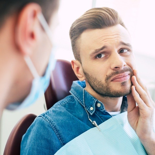 Man in need of impacted canine treatment holding jaw in pain