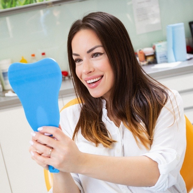 Woman looking at smile in mirror after facial cosmetic treatments