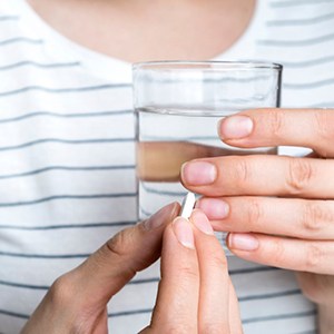Woman holding pill in one hand and water in the other
