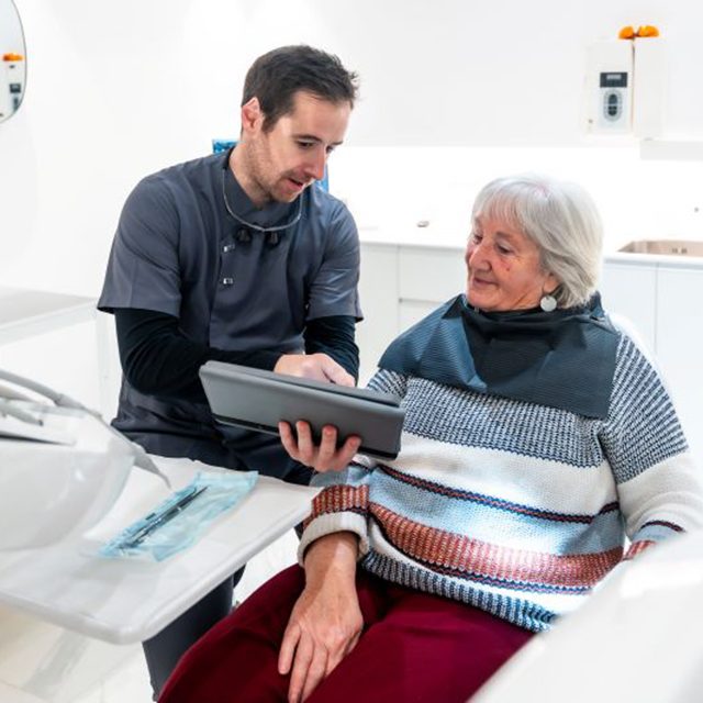Oral surgeon and senior patient looking at tablet
