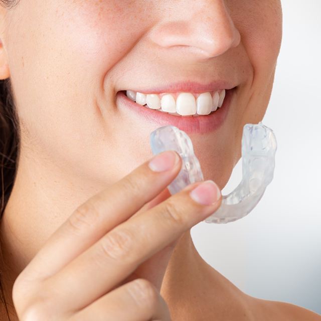 Smiling woman holding occlusal splint for TMD treatment