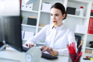 Woman with TMJ disorder chewing on pen while working