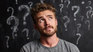 Man in front of chalkboard with question marks written all over it 